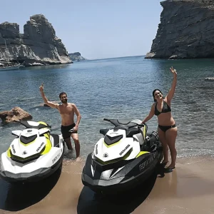Jet ski safari guests waving by their jet skis at a beach with rock formations