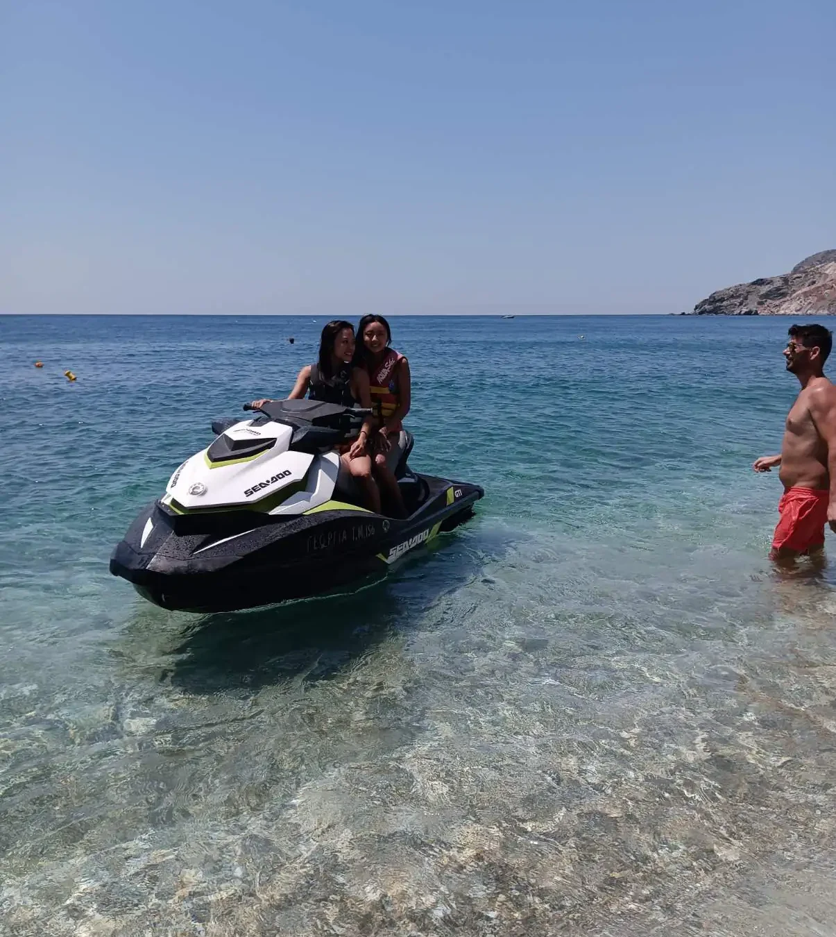 Two riders on a Sea-Doo jet ski in shallow clear water with their guide