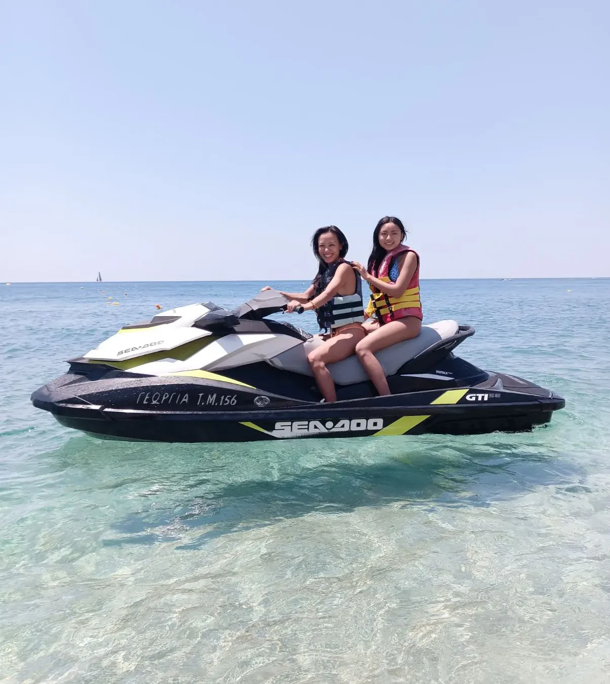 Two smiling riders on a Sea-Doo jet ski in crystal-clear water